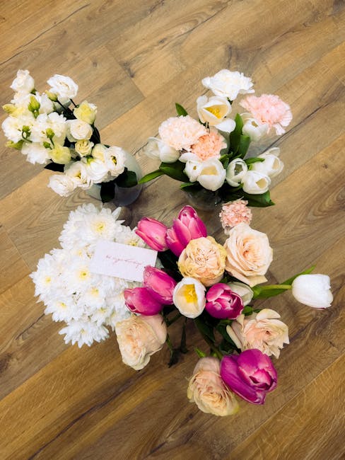 A collection of four floral arrangements placed on a wooden surface. The arrangement on the top left features small white flowers with green stems and leaves, wrapped in black floral paper. The top ri