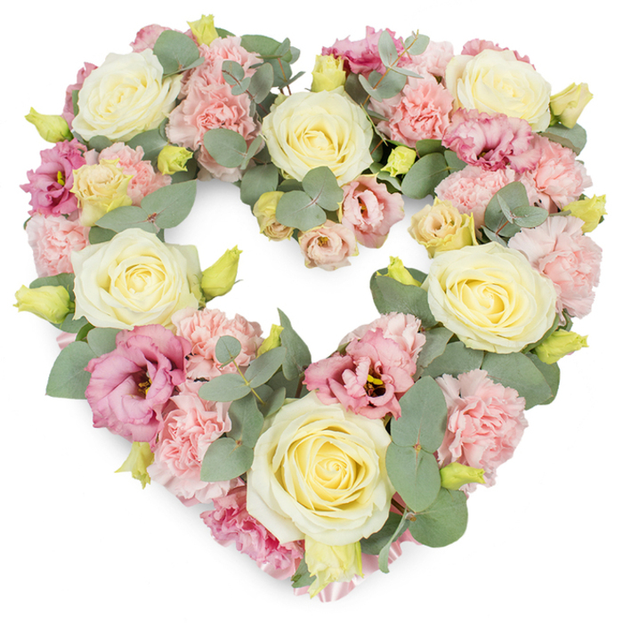 A beautifully composed heart-shaped wreath of sympathy flowers fills the image, set against a bright, uncluttered white background that allows every pastel tone and texture to stand out. Creamy ivory and pale yellow roses take pride of place, arranged at balanced intervals around the heart, their velvety petals tightly whorled at the centres and gently loosening toward the outer edges. Their elegant forms are softened by an abundance of light pink carnations, which create a delicate, frilled layer between the roses, like a soft blanket of petals. Among these, richer notes of colour appear in the form of mauve and deep rose-pink lisianthus, whose gracefully unfurling, slightly trumpet-shaped blooms and occasional darker centres add both depth and a touch of refined drama. Threaded throughout the flowers, slender stems tipped with small yellow-green buds signal freshness and vitality, as if the wreath had just been arranged in a Rush Green florist's studio ready for a family farewell. Cool, silvery-green eucalyptus leaves are artfully woven among the blossoms, their rounded shapes and smooth surfaces introducing a modern, airy touch that contrasts with the dense florals. The eucalyptus trails gently around the heart's outer edge, subtly tracing the symbolic shape and giving it a soft, natural frame. The wreath feels lush and complete, with no visible gaps, echoing the sense of a life remembered in full. This floral tribute would sit beautifully beside a coffin, on an easel at a memorial in Rush Green or Romford, or as a central piece at a remembrance gathering, conveying tenderness, sympathy, and a deep, abiding love for the person being honoured.